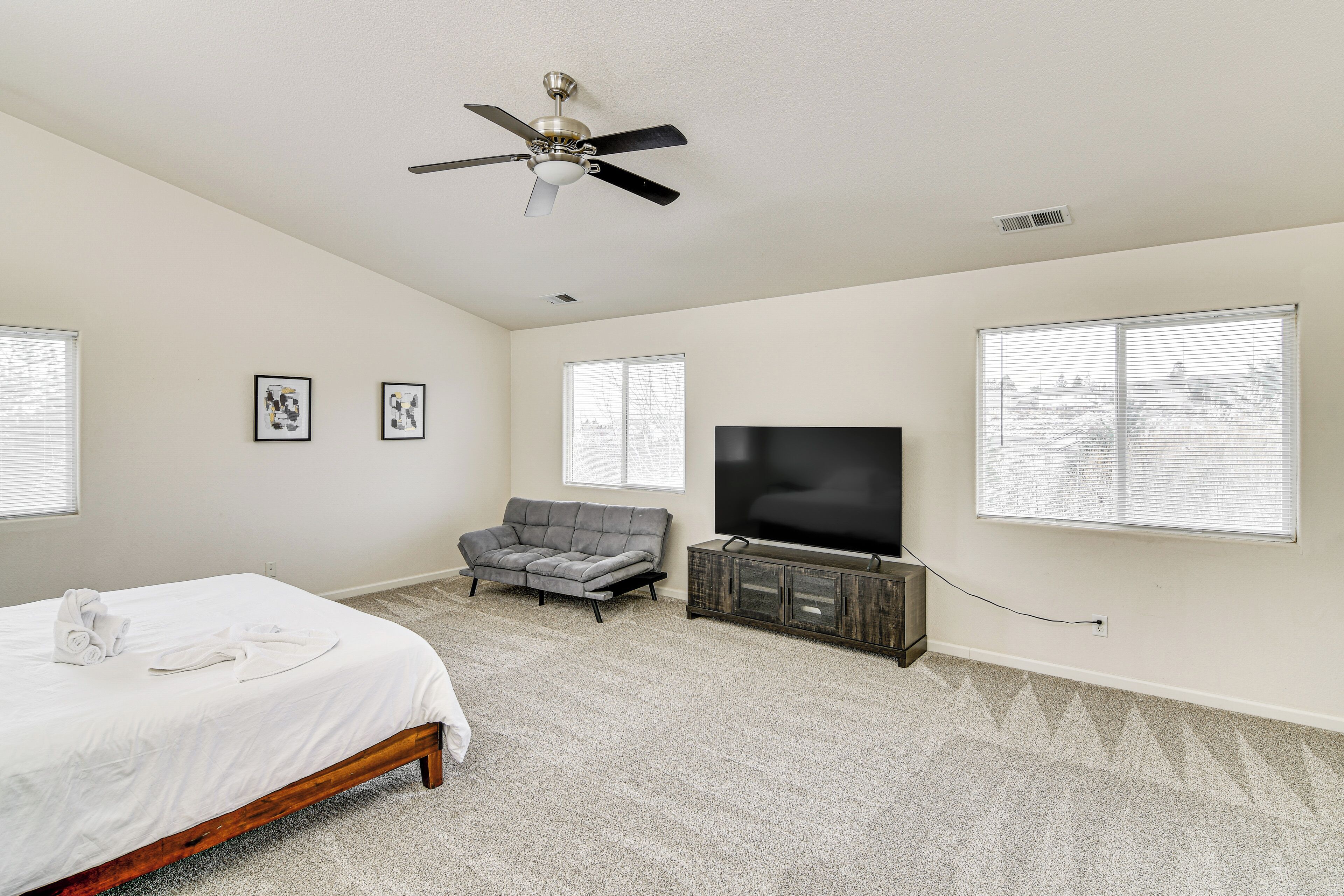 A bedroom with a bed, a gray sofa, a TV, and framed pictures on the wall.