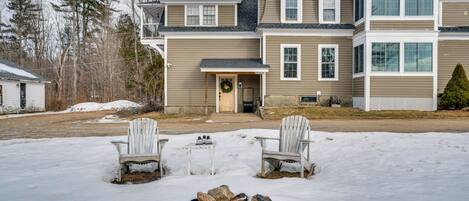 Ein zweistöckiges Haus mit Veranda, Kamin und zwei Adirondack-Stühlen.