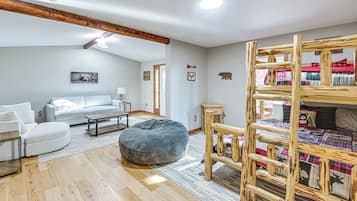Una sala acogedora con un sofá, un reposapiés y una cama nido de madera con un edredón acolchado.