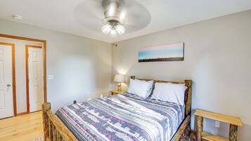 A bedroom with a wooden bed, a ceiling fan, a nightstand, a lamp, and a painting on the wall.