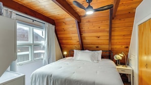 A bedroom with a wooden ceiling, a bed with white bedding, a nightstand with a lamp, and a wardrobe. - Red Lodge Cabin w/ Hot Tub ~ 1/2 Mi to Downtown! (Red Lodge)