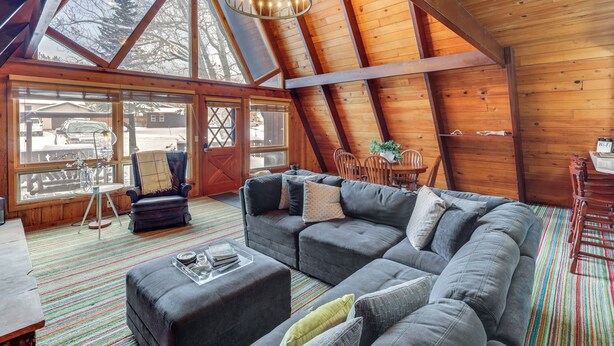 A spacious loft with a large sectional sofa, a dining area, and a view of the outside. - Red Lodge Cabin w/ Hot Tub ~ 1/2 Mi to Downtown! (Red Lodge)