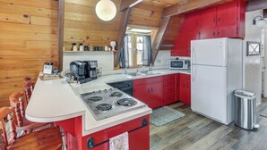 A kitchen with wooden walls, a white island with a stove, red cabinets, and a white refrigerator. - Red Lodge Cabin w/ Hot Tub ~ 1/2 Mi to Downtown! (Red Lodge)