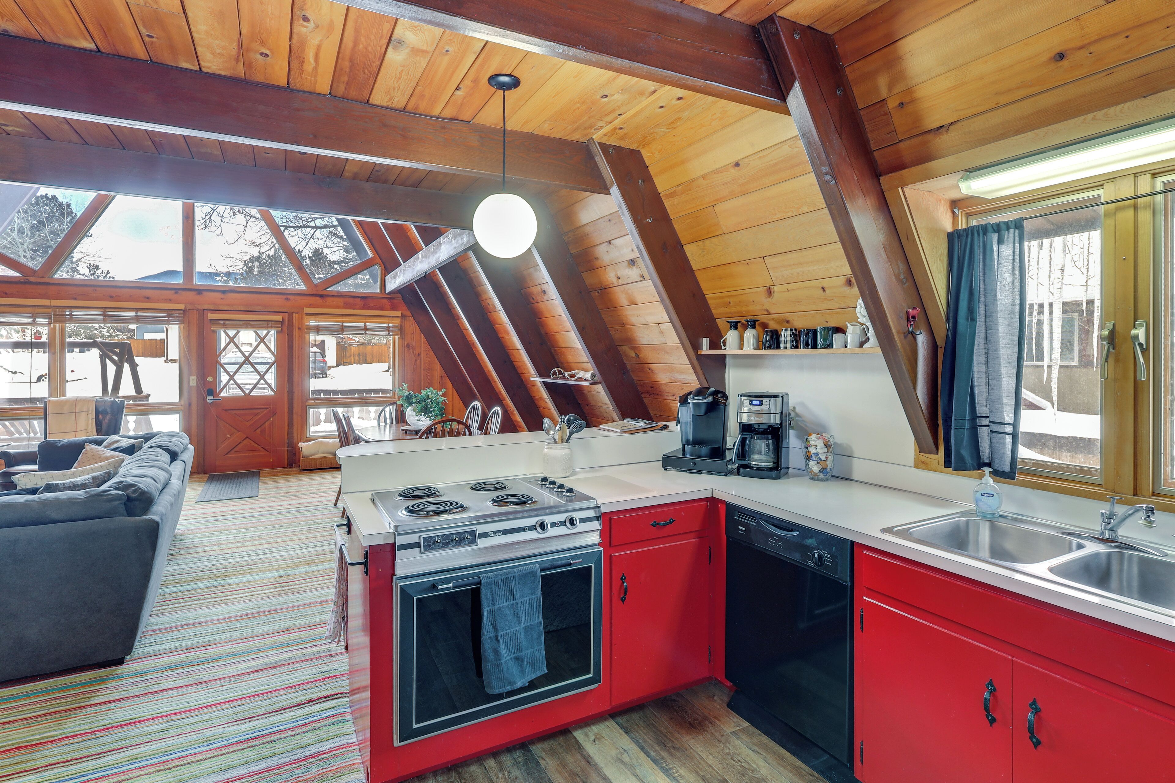 Une cuisine moderne avec des meubles rouges, une cuisinière et un lave-vaisselle. Une grande fenêtre offre une vue sur l’extérieur.