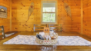 A wooden cabin interior with a dining table set with a basket of food items, a coffee cup, and a menu.