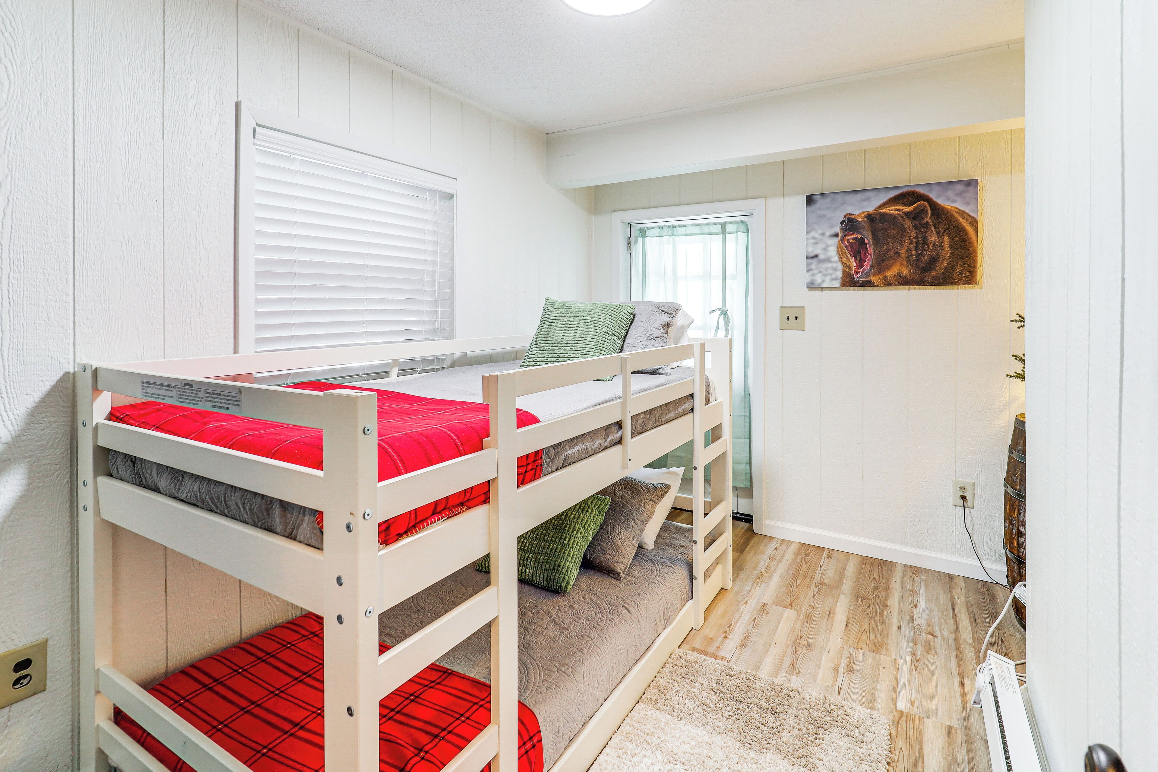 Une chambre avec un lit superposé, une fenêtre, une porte et un tableau représentant un ours accroché au mur.