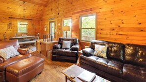 A cozy cabin interior with wooden walls, leather furniture, and large windows offering natural light.