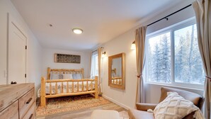 Een slaapkamer met een houten bed, een dressoir, een raam met uitzicht op besneeuwde bomen en een spiegel aan de muur.