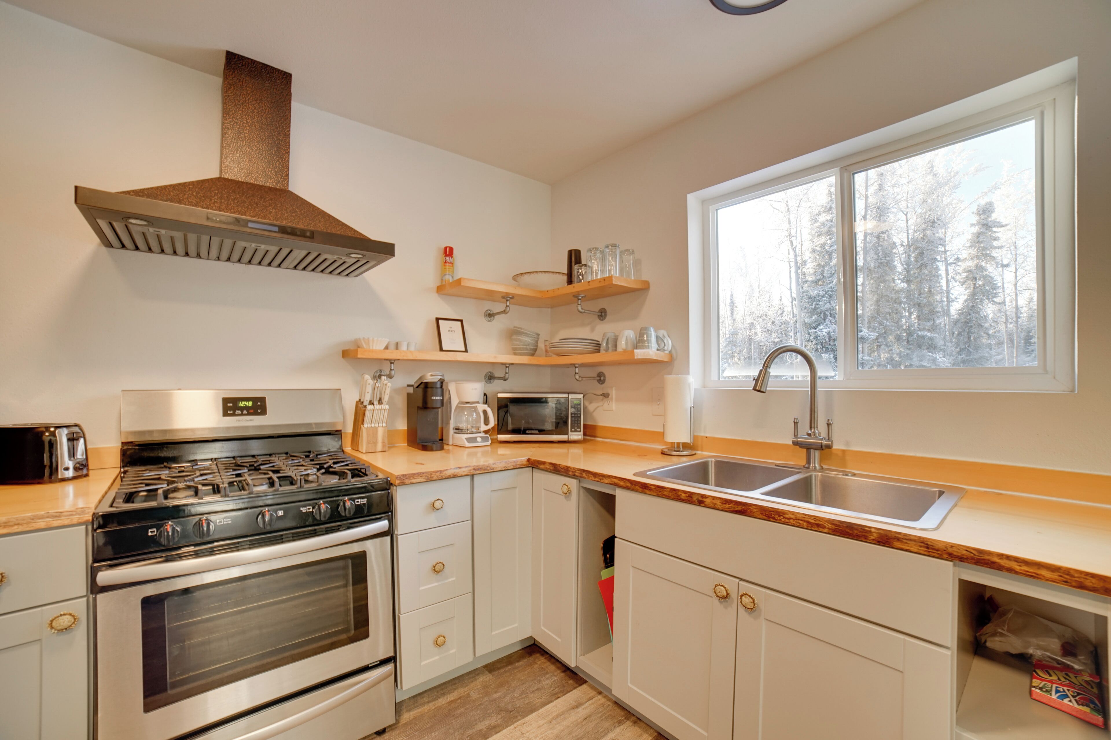 A modern kitchen with white cabinets, a stainless steel stove, a microwave, and a large window with a view of trees.