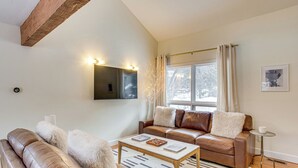 A modern living room with a brown leather sofa, a wooden coffee table, and a large window with curtains. - Par & Powder: Avon Haven w/ Golf & Ski Access! (Avon)