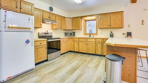 Una cocina con armarios de madera, refrigerador, microondas, estufa y un bote de basura.