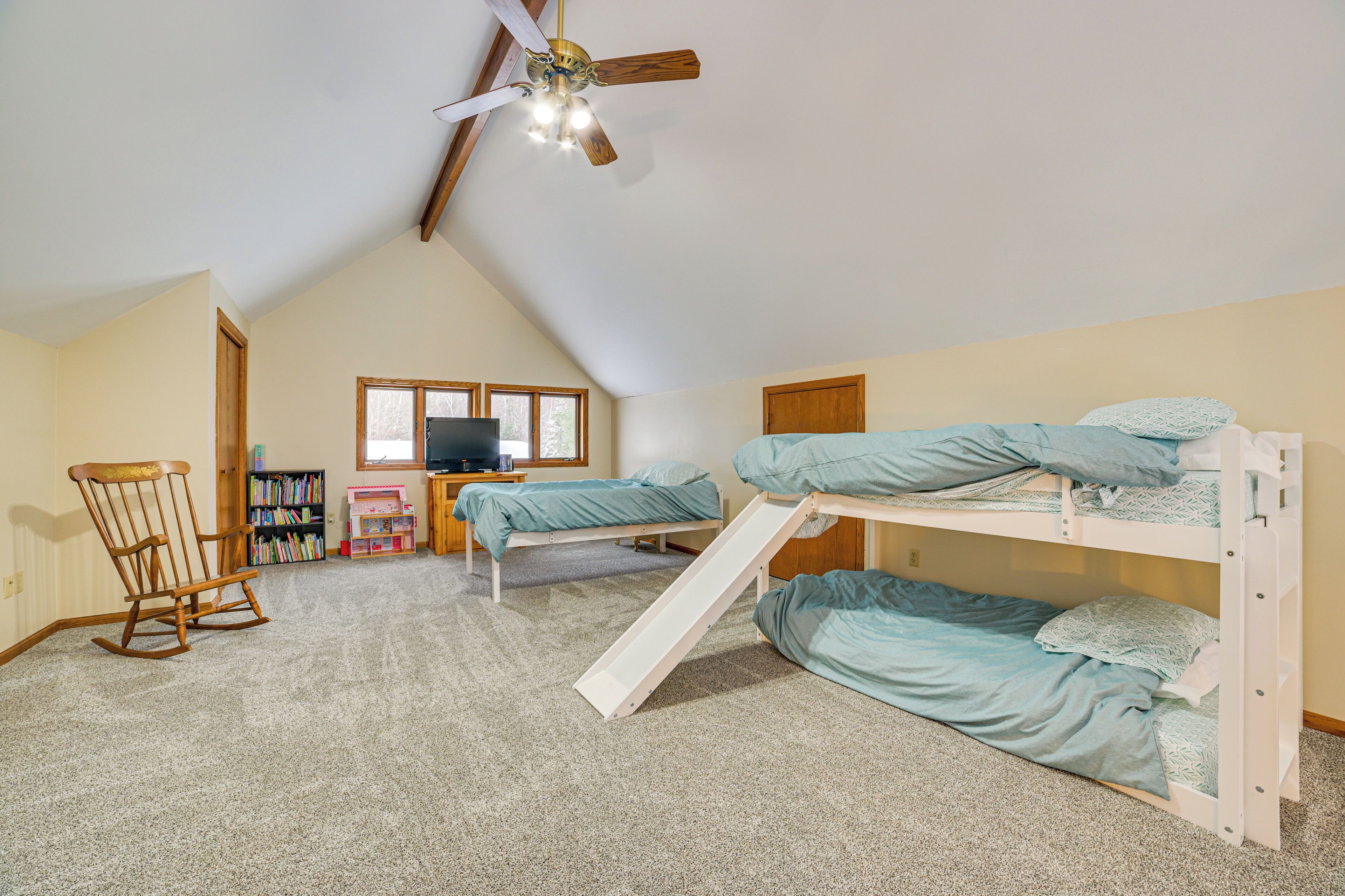 A bedroom with bunk beds, a ceiling fan, a bookshelf, and a window.