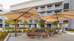 Ein moderner Außenbereich mit Sitzgelegenheiten, darunter eine Couch, Stühle und ein Tisch, umgeben von großen Sonnenschirmen und Pflanzen.
