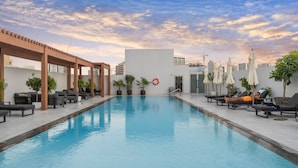 Ein Schwimmbecken mit Liegestühlen und Sonnenschirmen, umgeben von Blumentöpfen und einer Pergola.