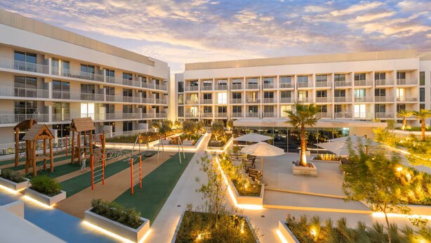 Ein mehrstöckiges Hotel mit Balkonen, einem Spielbereich für Kinder, Außenbestuhlung und angelegten Gärten.
