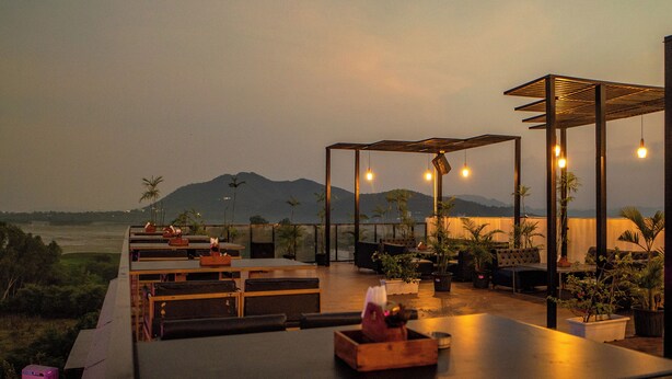 An outdoor seating area with tables and chairs, potted plants, and a view of distant mountains. - THE COURTYARD - Beyond Bar & Club (Udaipur)