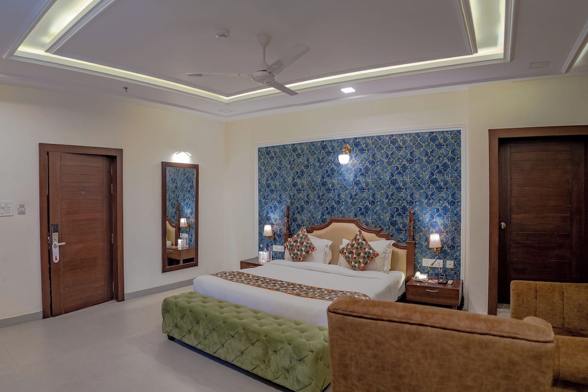 Habitación de hotel con una cama grande, un banco tapizado en verde, un sillón marrón y un ventilador de techo.