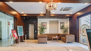 A modern lobby with a chandelier, a sofa, a coffee table, and a reception desk. - THE COURTYARD - Beyond Bar & Club (Udaipur)