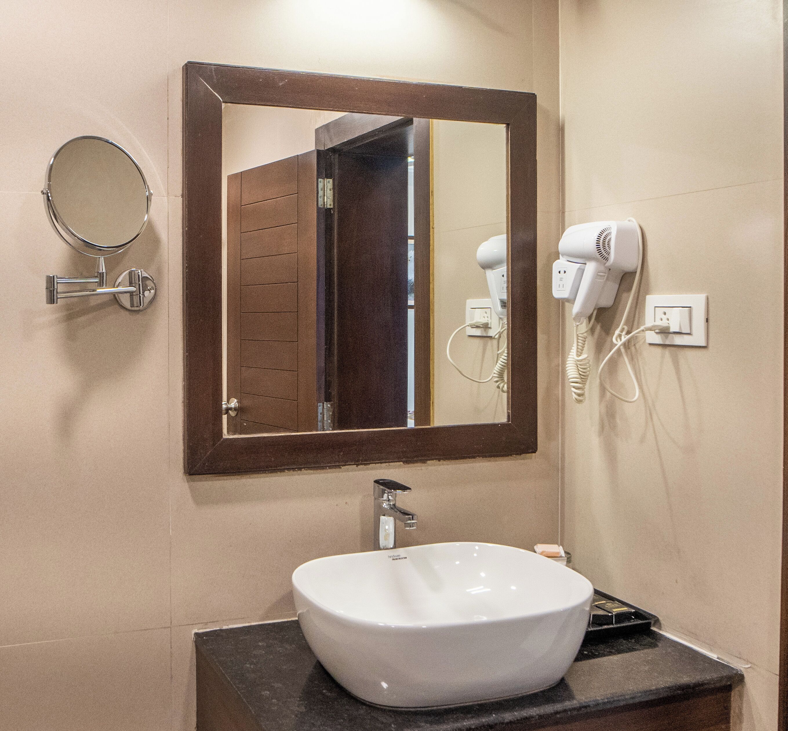 Un baño con un espejo redondo, un espejo rectangular, un lavabo blanco, un secador de pelo y un toallero.