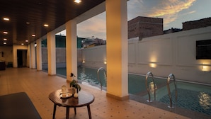 A pool area with a table and chairs, a poolside view, and a brick wall. - THE COURTYARD - Beyond Bar & Club (Udaipur)
