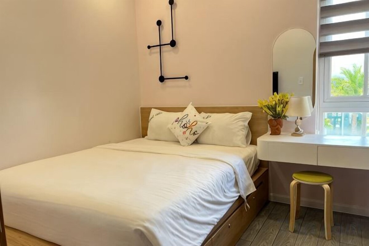 A bedroom with a bed, bedside table, mirror, and window.