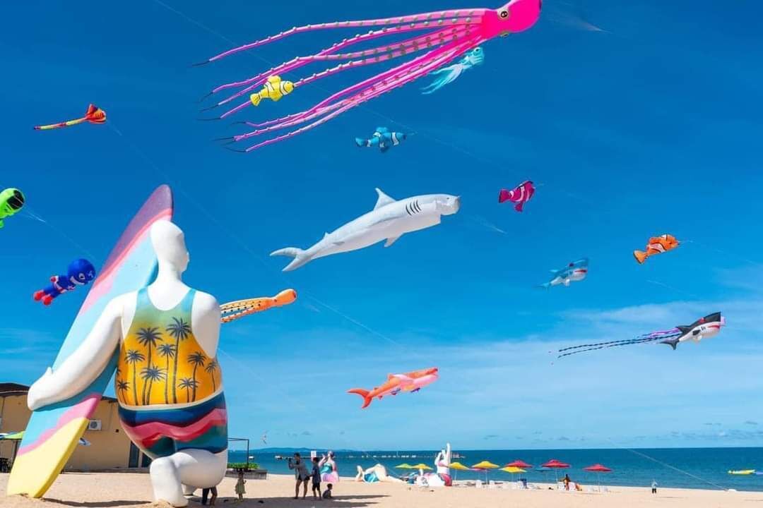 A beach with colorful kites, including octopus and shark shapes, and a lifeguard statue.