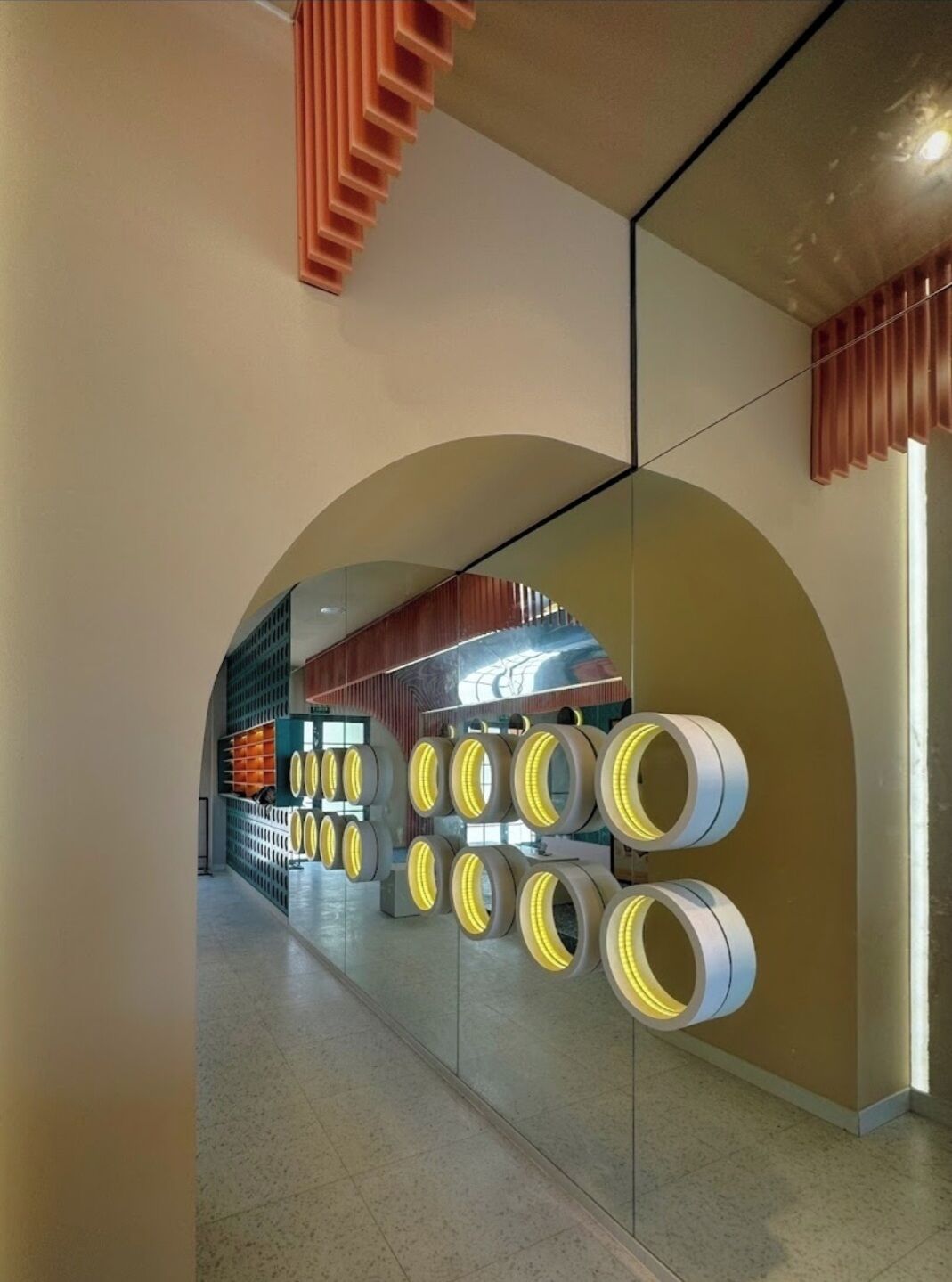 Un intérieur moderne avec un mur incurvé en verre, un plafond à lattes de bois et une série d’objets circulaires éclairés.