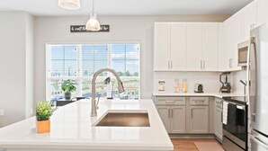 A modern kitchen with white cabinetry, a large island with a sink, and stainless steel appliances. - Reluxme|Chic  2BR w/ Balcony, Gym & Pool Near Mall (Charlotte)