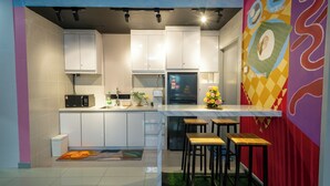 A modern kitchen with white cabinets, a refrigerator, a microwave, and a sink. There are three wooden stools at the counter.
