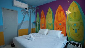 A hotel room with a bed, a nightstand, and a wall with colorful surfboard murals.