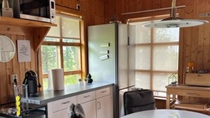 Una cocina compacta con paredes de madera, un refrigerador, un microondas y un lavamanos. Hay una mesa redonda con sillas y una lámpara colgante.
