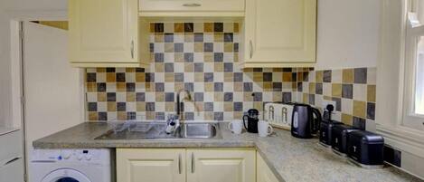 A compact kitchen with a washing machine, a sink, a toaster, and a coffee maker.