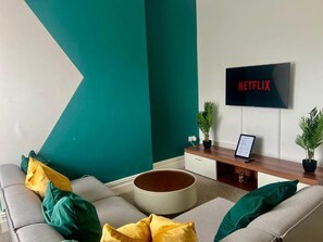 A living room with a sofa, pillows, a coffee table, a TV mounted on the wall, and a small plant on the side table. - 2 Bed Flat - Sleeps 5 - Pets - Parking - Wifi (Leicester)