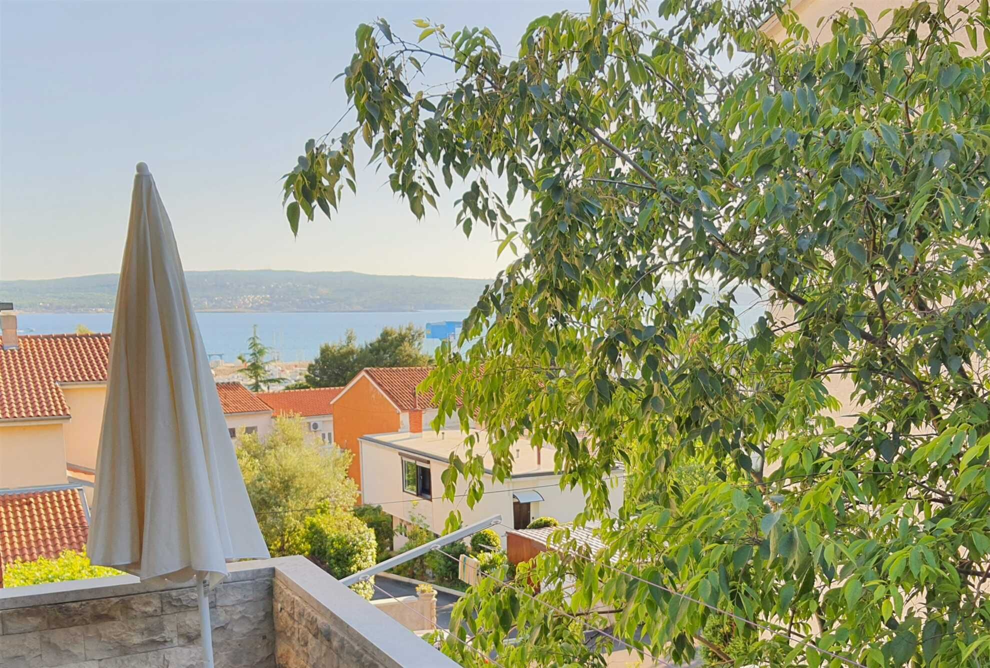 A balcony with a view of a coastal town, a clear sky, and a body of water in the distance.