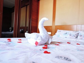 Un lit décoré d’une serviette en forme de cygne et de pétales de rose.