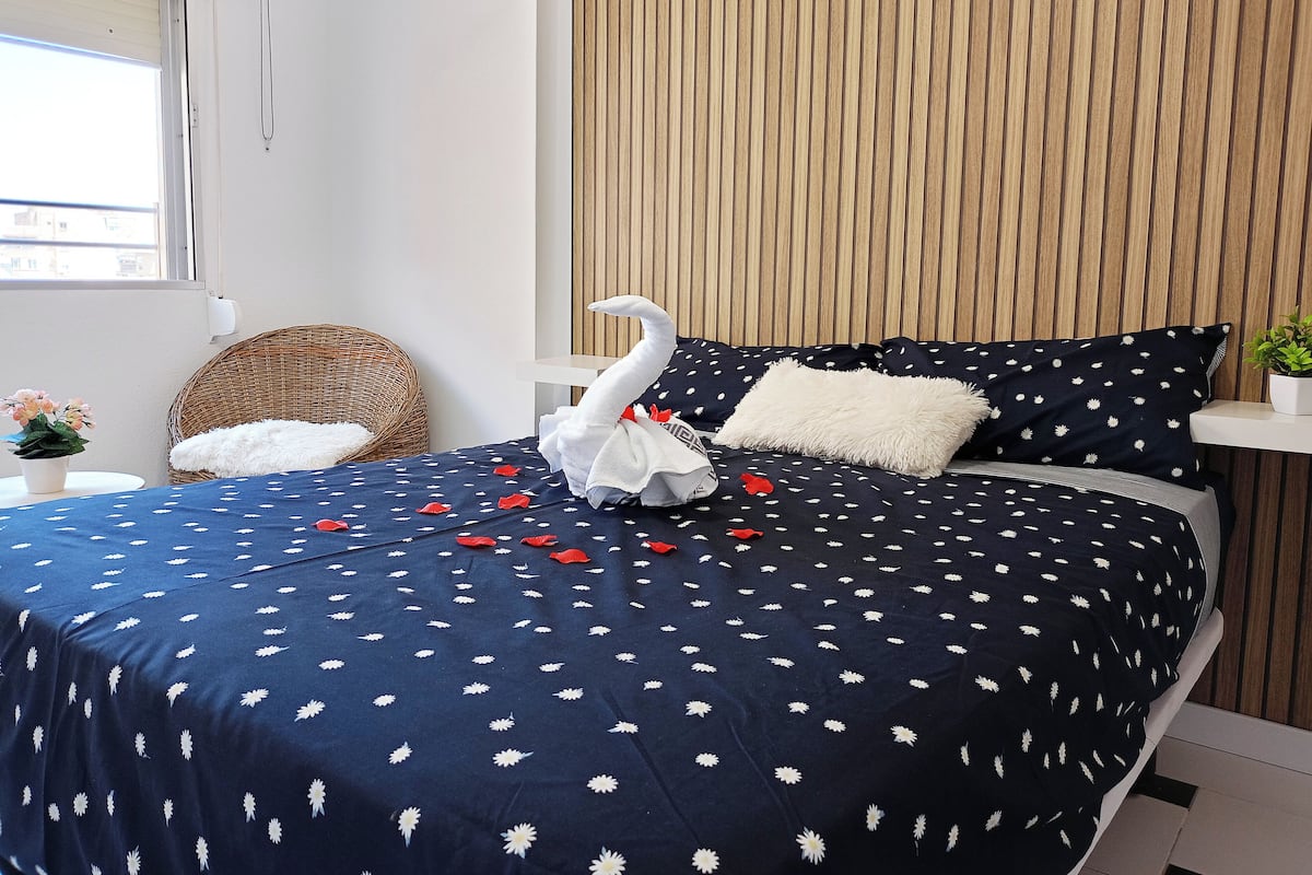 En snyggt bäddad säng med ett mörkblått, blommigt sängöverkast, en vit, fluffig kudde och en dekorativ, vit svanfigur.