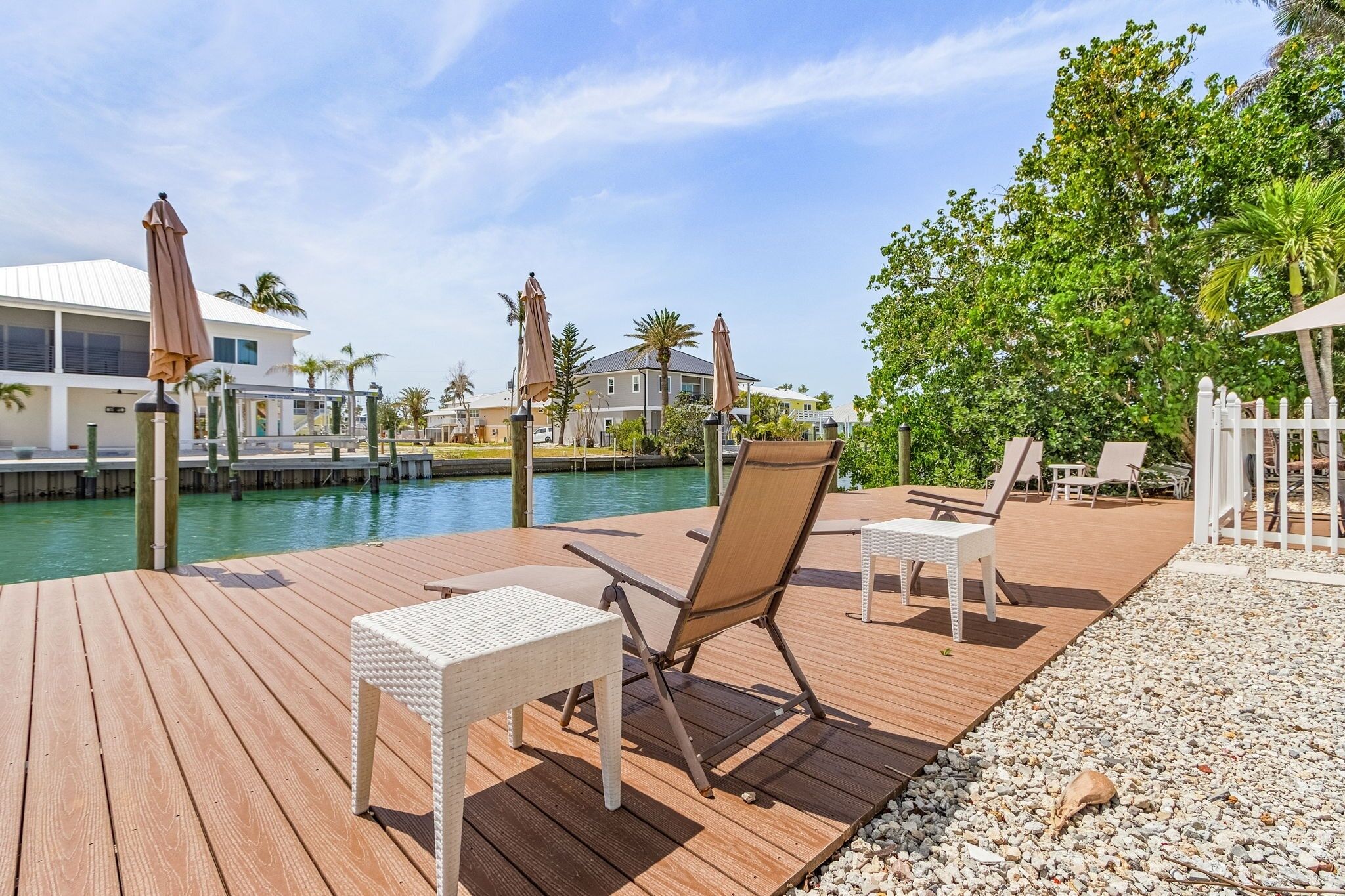 A wooden deck with lounge chairs and umbrellas overlooking a body of water, with buildings and greenery in the background.