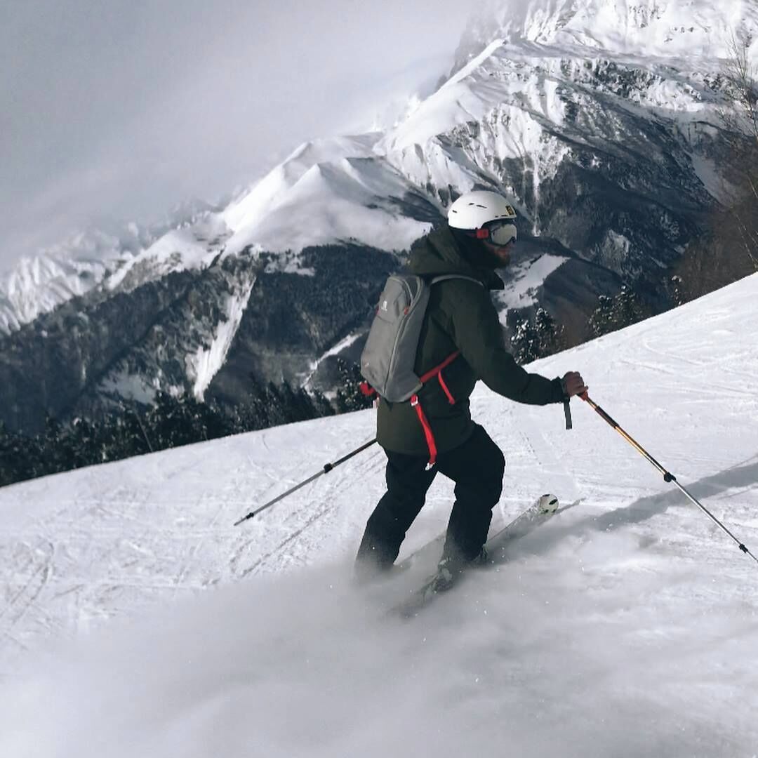 A person skiing on a snowy slope with mountains in the background.