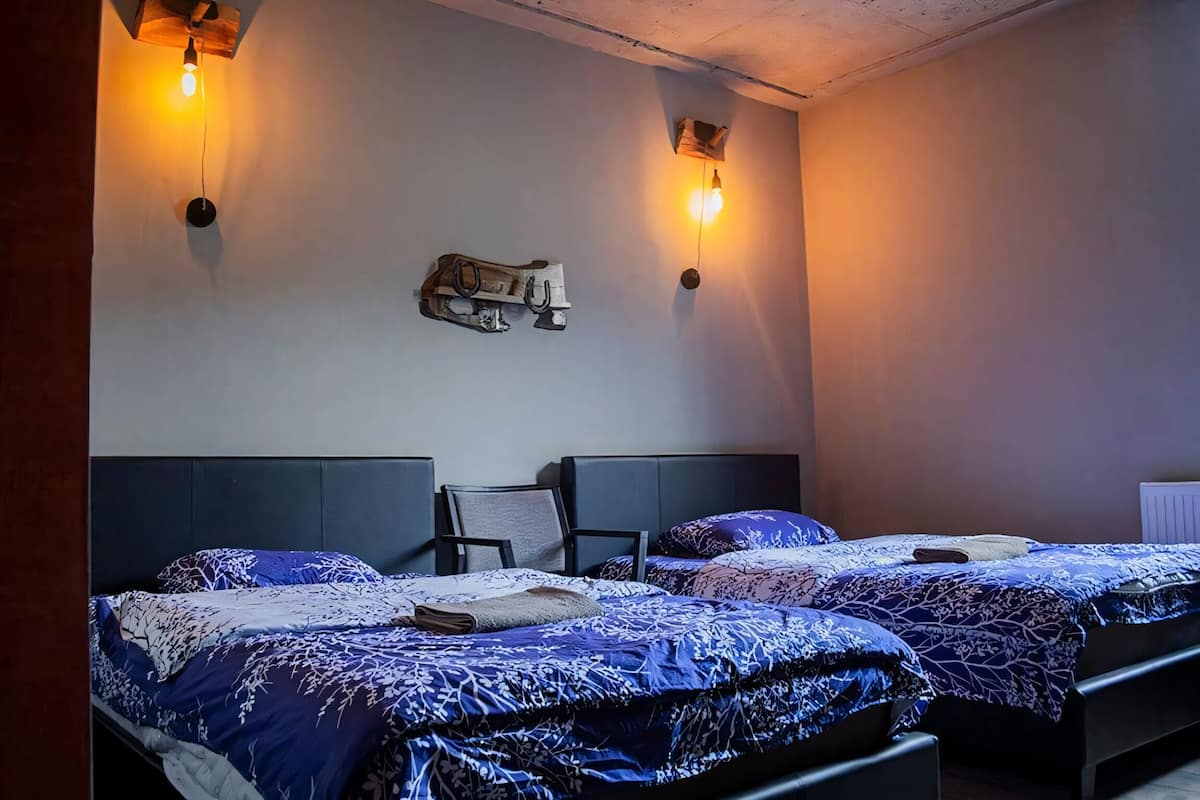 Ett hotellrum med två sängar, där varje säng har mönstrat sänglinne, en stol och väggmonterade lampor.
