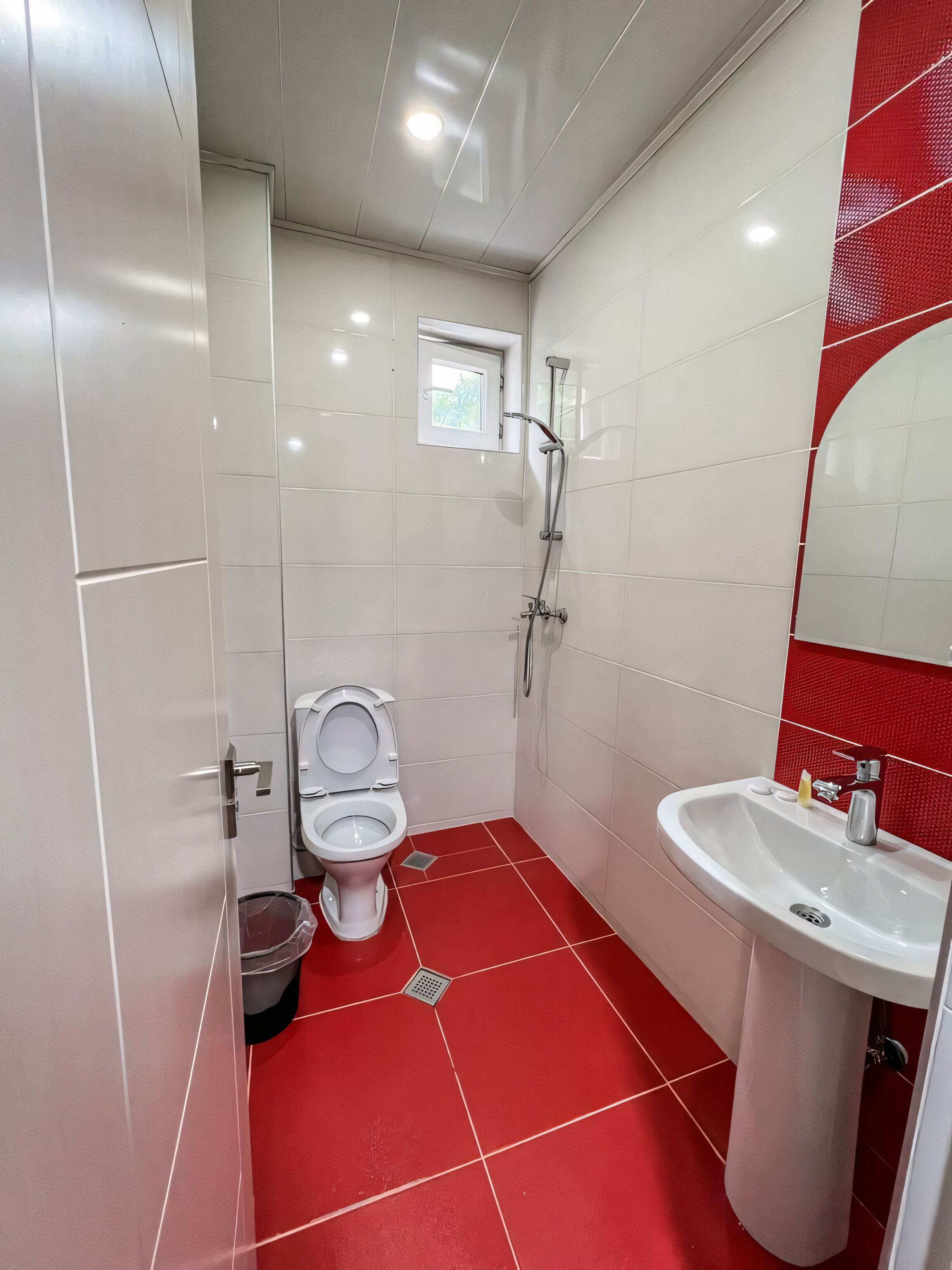 Ein modernes Badezimmer mit weißen und roten Fliesen, einer Toilette, einer Dusche und einem Waschbecken.