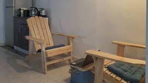 A compact kitchen with a refrigerator, toaster, kettle, and a blue storage bin. There are two wooden chairs and a small table with a cushion. A framed picture hangs on the wall. - Village house close to the lagoon and the sea (Marseillan)