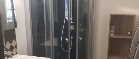 A corner shower enclosure with a glass door, a white sink, and a tiled floor.