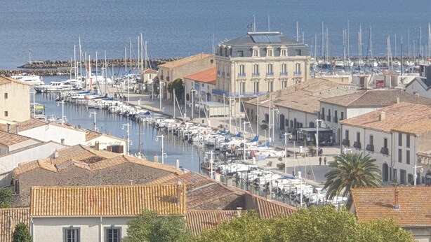 A marina with boats docked along the waterfront, surrounded by buildings with traditional architecture. - Village house close to the lagoon and the sea (Marseillan)