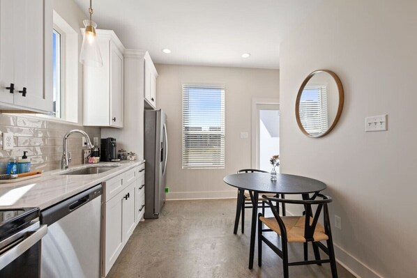 A modern kitchen with white cabinets, a stainless steel refrigerator, a dishwasher, and a dining area with a round table and chairs.