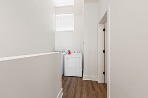 Une buanderie équipée d’un lave-linge et d’un sèche-linge, avec un plancher en bois et des murs blancs.