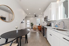 Une cuisine moderne avec des meubles blancs, une table à manger noire et un ventilateur de plafond.