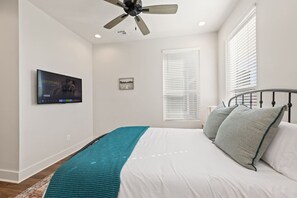 A bedroom with a bed, a ceiling fan, a TV mounted on the wall, and a window with blinds. - NEW-Swamp House-Luxury Amenities-65` TV-Fast WiFi (Lafayette)