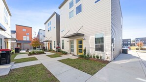 Una hilera de casas adosadas modernas con un paseo central, jardines delanteros y un estacionamiento.
