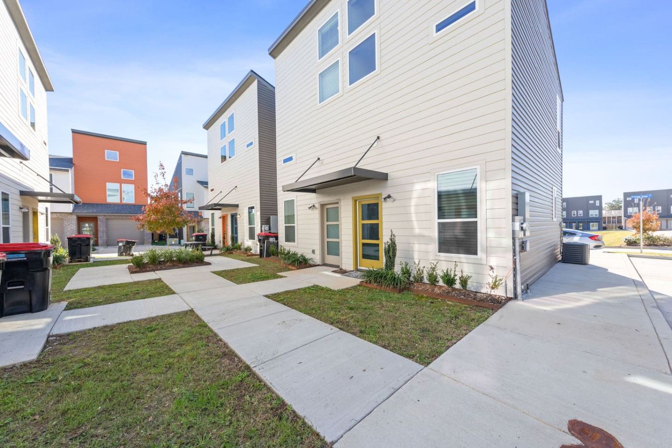 A row of modern townhouses with a central walkway, front yards, and a parking area.