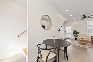 A modern living room with a round dining table, two chairs, a round mirror, a ceiling fan, and a potted plant.